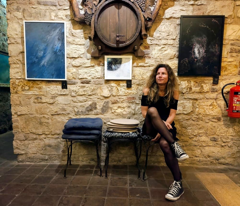 Kateřina Murová sedící pod svými obrazy ve vinném sklepě